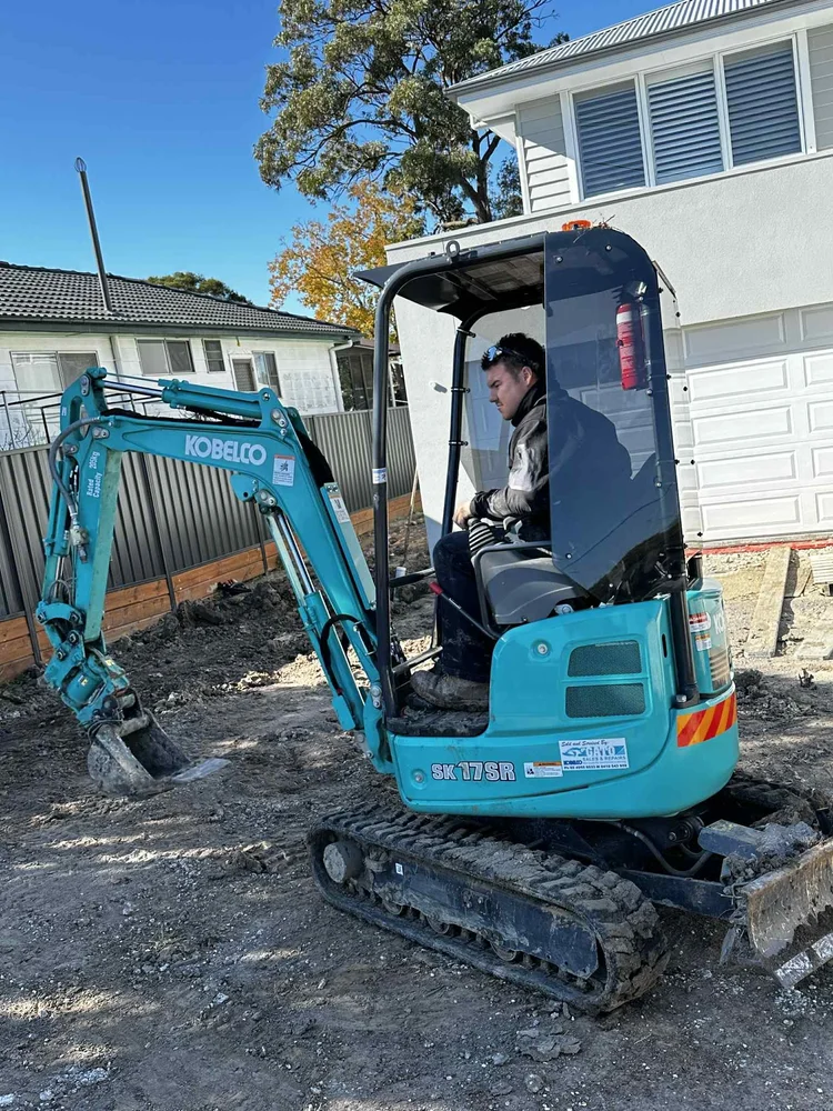 Operator running a small blue excavator on a construction site
