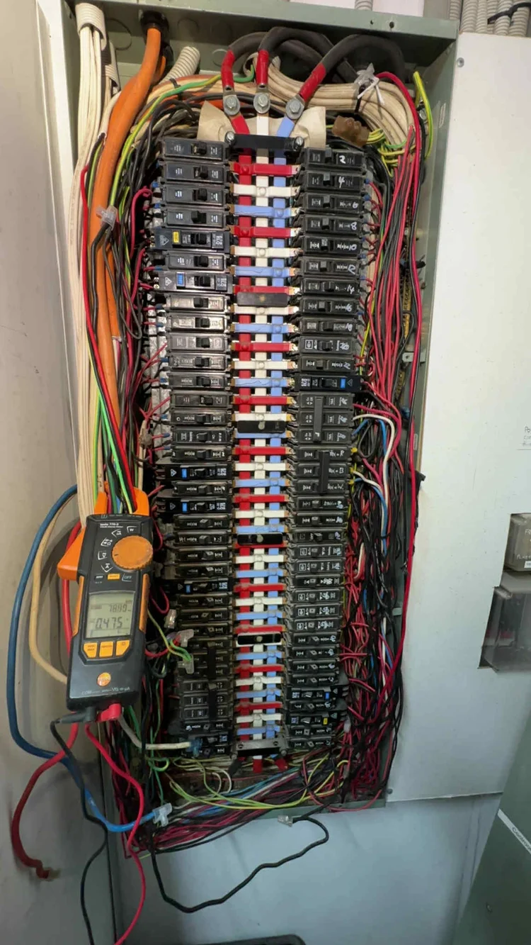 Open electrical panel with multiple circuit breakers and coloured wires