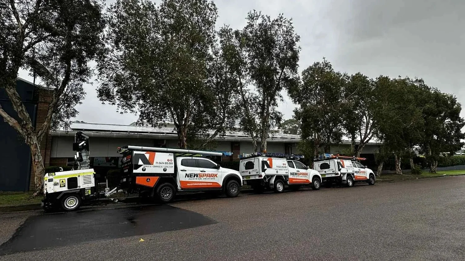 Three utility trucks parked in a row on wet asphalt under grey skies