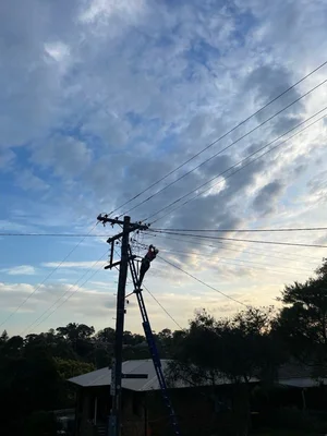 An electrician on a ladder repairing power lines on a utility pole